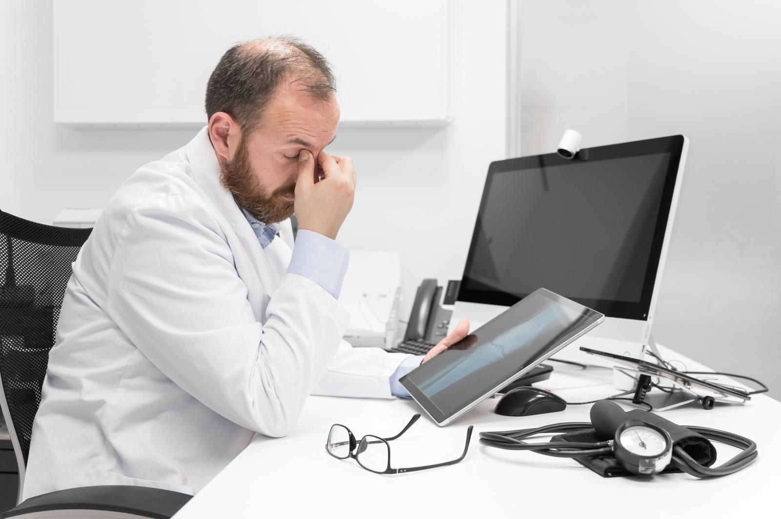young doctor rubbing his eyes, feeling tired and unhappy. health care worker stress and frustration concept